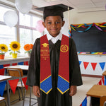 Young boy in graduation attire standing in a classroom with decorations.